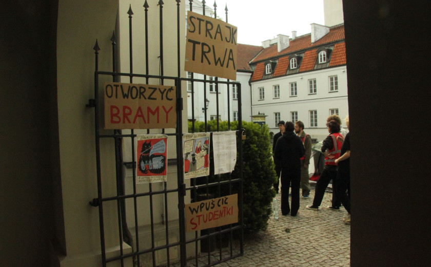 Slika železnih vrat a, ki vodijo na dvorišče stavbe Študentskega sveta Univerze v Varšavi. Na vratih so protestni slogani zasedbe.