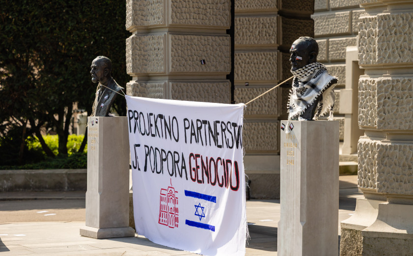 Slika z majskega protesta LDŠ pred rektoratom Univerze v Ljubljani. Na sliki je za doprsna kipa obešena zastava, na kateri piše "Projektno partnerstvo je podpora genocidu". Pod napisom sta narisana logotip Univerze v Ljubljani in izraelska zastava.